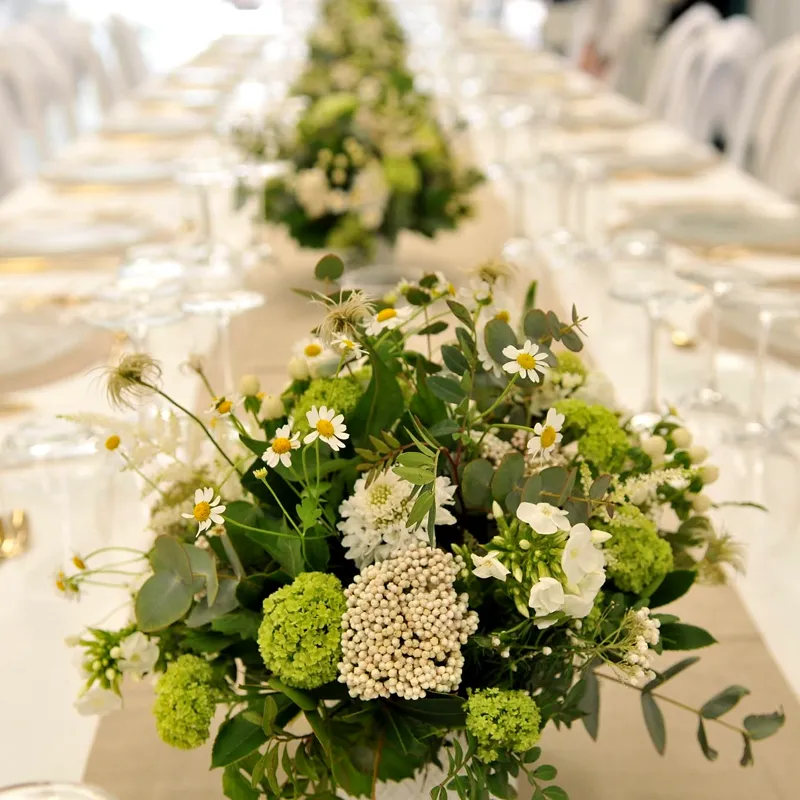 Mesa con mantel blanco, copas y centros de flores blancas y verdes